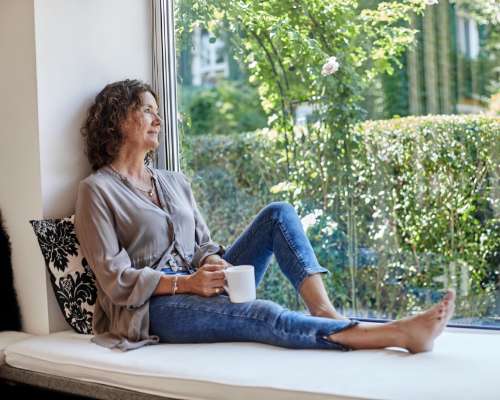 A woman sits in a large window and drinks some tea