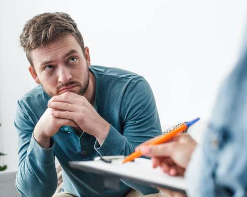 A young man holds his head in his hands while listening to a counselor