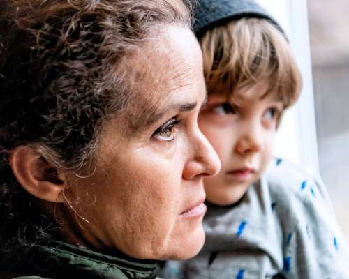 A woman and child look with serious faces out a window