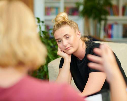 A young woman leans her head in her hand while listening to a counselor