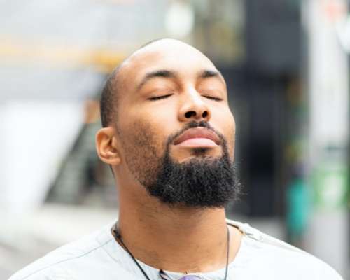 A black man closes his eyes and faces the sky into the sun light