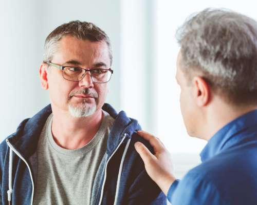 A counselor places his hand on a patient's shoulder to console him.