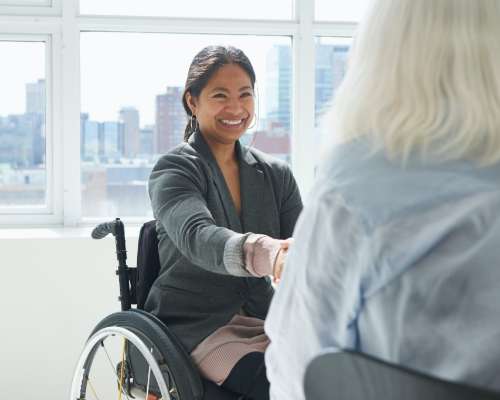 A woman in a wheel chair shakes hands with another person