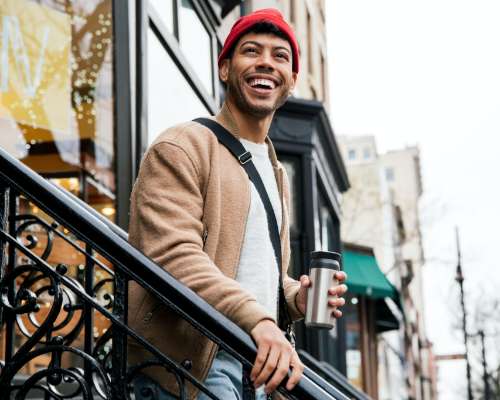 A man in an orange cap smiles from his city walkup stoop.