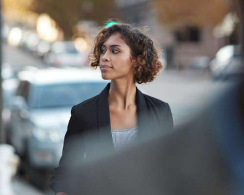 A young woman dressed in a suit walks down the city sidewalk