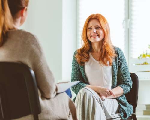 A counselor with red hair speaks to a patient across the room